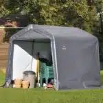 Skladiščni šotor 24x24m sive barve na travnati podlagi z vrtnim orodjem