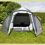 Odprti vhod šotora za kampiranje Coleman Crestline 3 z razkritim pogledom na notranji prostor prikazan v naravnem okolju s cvetočim vrtom v ozadju kar poudarja prijetno vzdušje za kampiranje