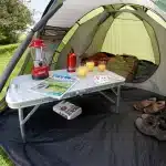 Kamp oprema kot so svetilka pijače in igralne karte so prikazani znotraj šotora Coleman Darwin 2+ kar ilustrira prijetno in domače kamp okolje