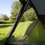 Odprt pogled iz šotora Coleman Darwin 2+ na zelen travnik ki povezuje bivanje v šotoru z občutkom odprtosti do okolja