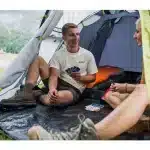 Mlad par sedi v šotoru Coleman Darwin 3+ in igra karte kar prikazuje prostorno in udobno notranjost šotora