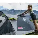 Ženska postavlja šotor Coleman Darwin 3+ z gorskimi vrhovi v ozadju kar poudarja lahkotnost postavitve in avanturistični duh