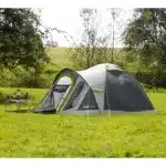 Šotor Coleman Darwin 4+ postavljen na zelenici s kamp opremo ob strani ki kaže pripravljenost za udobno kampiranje v naravi