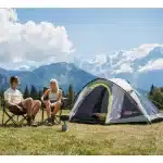 Par sedi pred šotorom Coleman Darwin 4+ na idilični kamp lokaciji z gorskim razgledom kar poudarja šotorjevo povezavo z avanturističnim kampiranjem