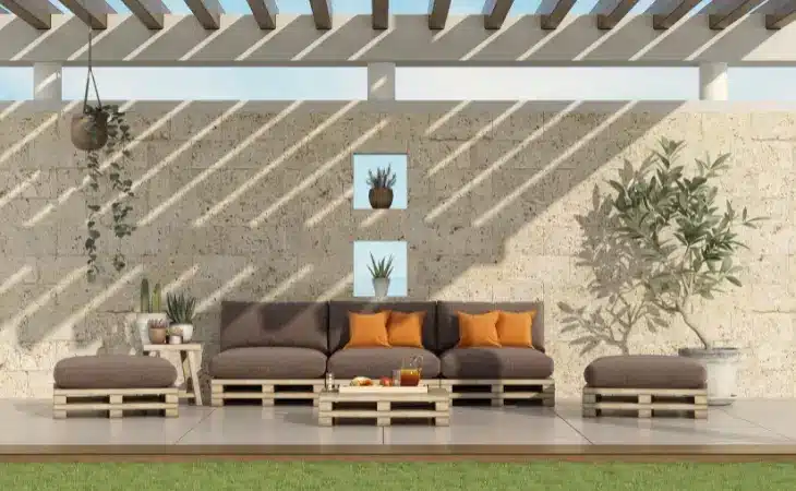 Vrtni kavč iz pelet na zasenčeni terasi v rjavi barvi z oranžnimi blazinami.