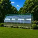Curved transparent greenhouse in a well kept backyard with vented side panels and well manicured plants around it