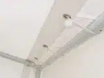 Close up of a white curtain track with cords and small white ball finials along the ceiling beam