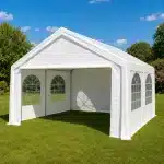 White outdoor event tent with arched window panels set up on a green lawn under a blue sky