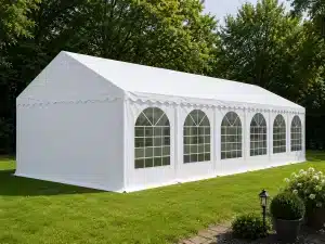 White event tent on a grassy lawn with arched window sides and decorative scalloped edge set among trees