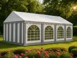 Large white and gray striped event tent with arched clear windows set up on a lawn with pink flowers in the foreground