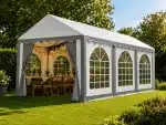 White outdoor event tent with arched windows and string lights set for a garden dinner