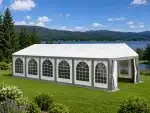 White event tent set up on a grassy lawn by a lake with mountains in the background