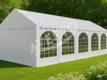White event tent with arched windows set up on a grassy lawn outdoors It has a peaked roof and scalloped valance along the top edge