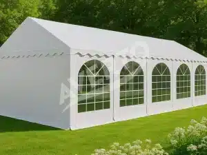 White event tent with arched windows set up on a grassy lawn outdoors It has a peaked roof and scalloped valance along the top edge