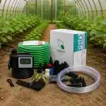 Drip irrigation kit laid out on soil in a greenhouse with timer green hose tubing and fittings beside a boxed system