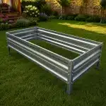 Rectangular galvanized metal raised garden bed on a lawn in a backyard of flowers and plants in the background