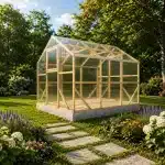 Wood framed glass greenhouse on a concrete base in a lush garden with blooming flower beds nearby